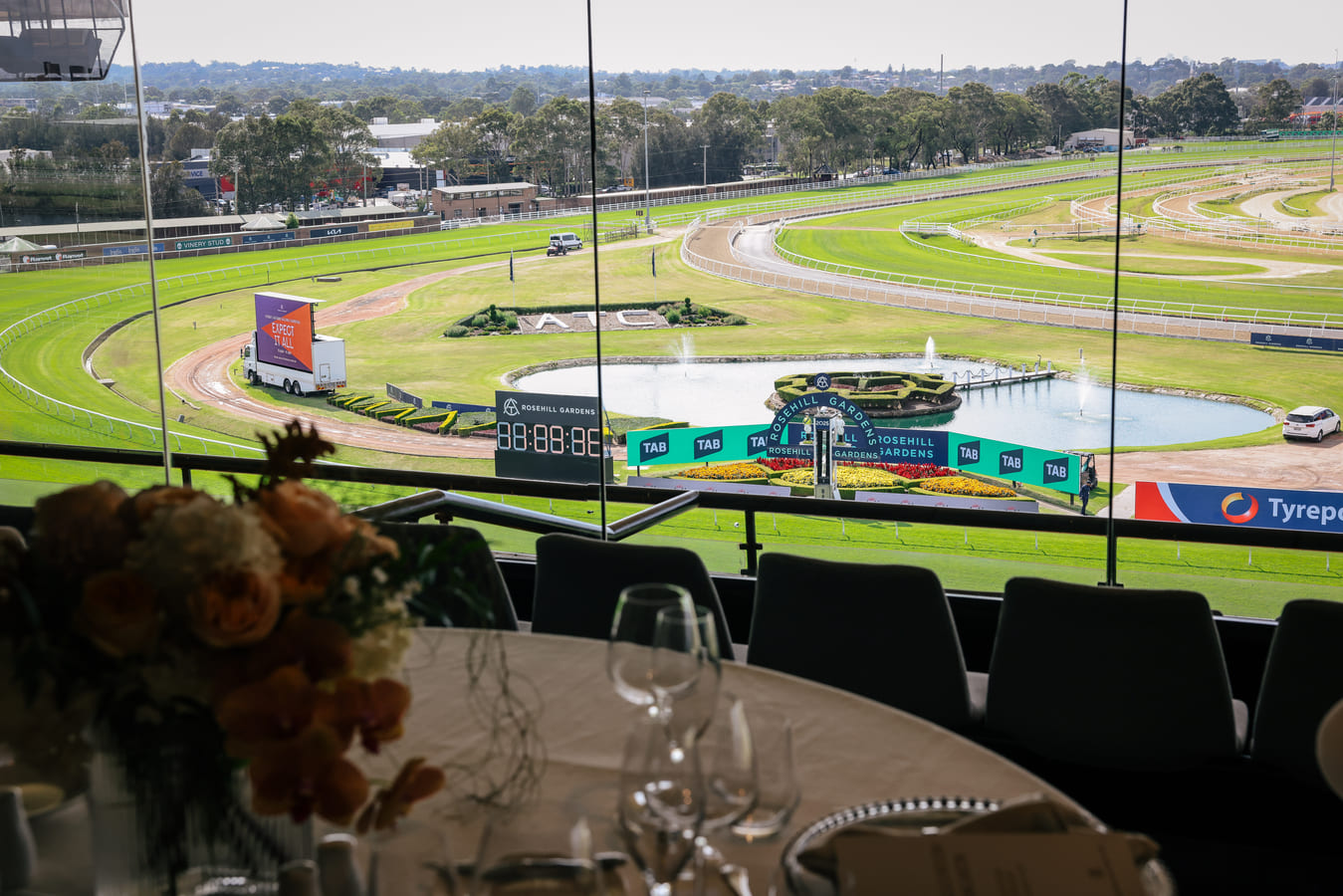 Empty seating in a restaurant within a racecourse grandstand, with tall windows looking out to the track below