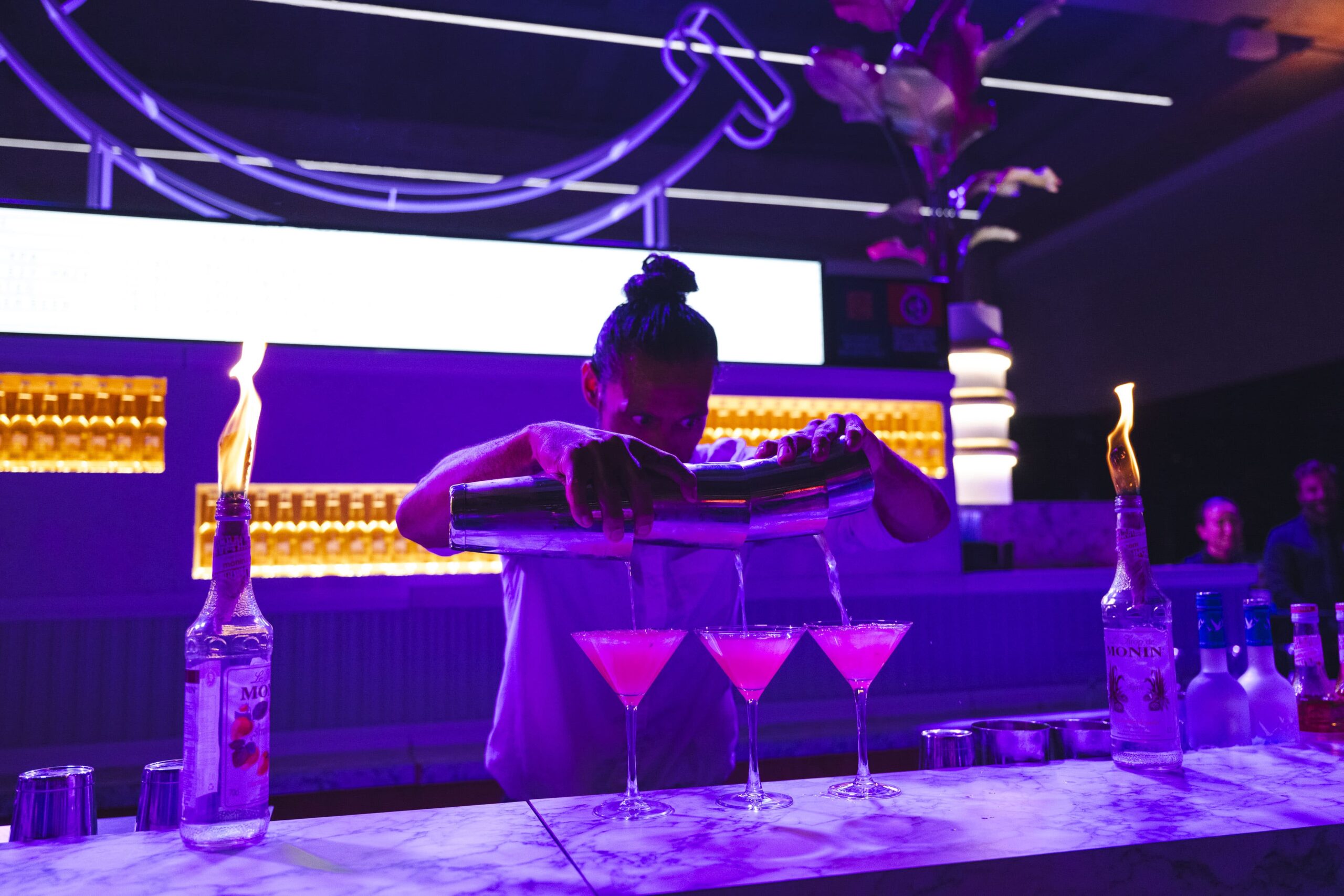 A bartender prepares cocktails at an event, as flames emerge from nearby bottles of alcohol